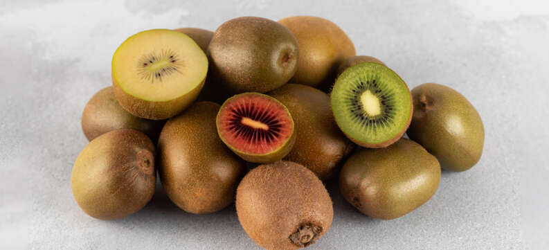Different varieties of kiwi lie in a pile on the table. Halves of red, yellow and green kiwi. Different varieties of kiwi lie in a pile on the table. Halves of red, yellow and green kiwi. Fruit varieties.